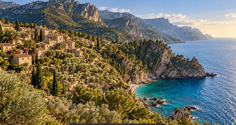 Kamnita vasica nad turkiznim zalivom na Mallorci, z gorami Serra de Tramuntana v ozadju.