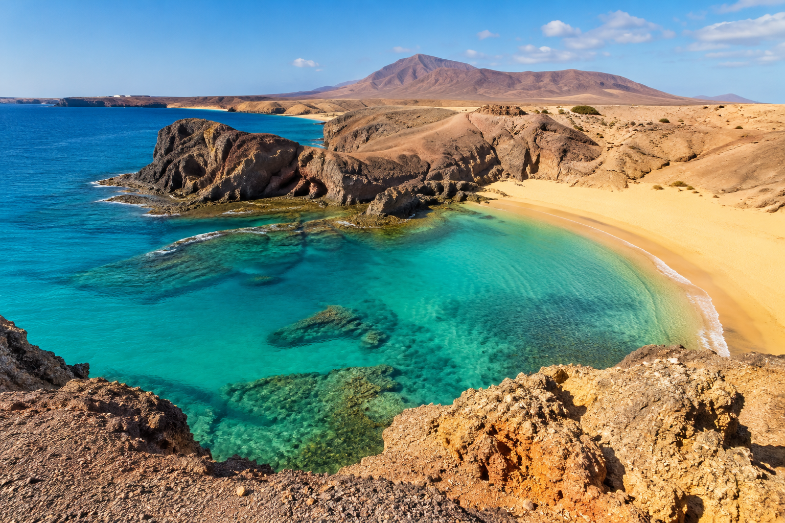 Peščena plaža s turkiznim morjem in vulkansko pokrajino na Lanzarotu.